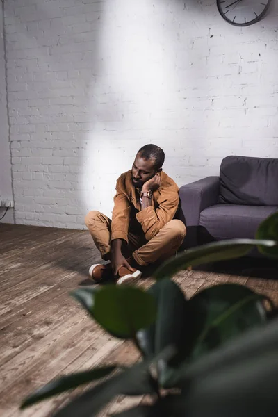 Focus selettivo dell'uomo afro-americano seduto sul pavimento e che tocca il viso — Foto stock