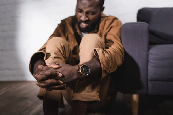 Селективный фокус африканского американца, сидящего на полу с сжатыми руками — стоковое фото