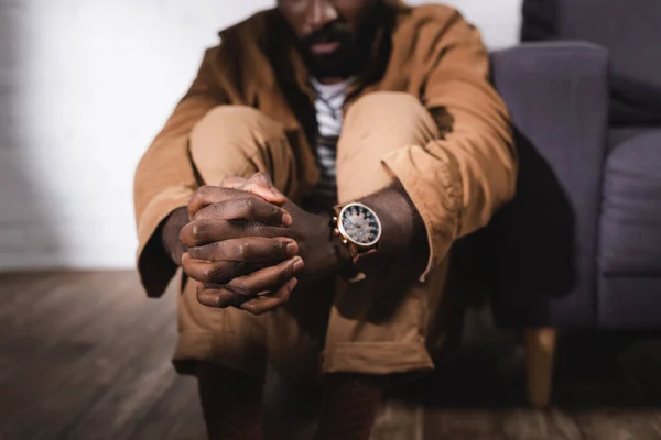 Cropped view of african american man sitting on floor with clenched hands — Stock Photo