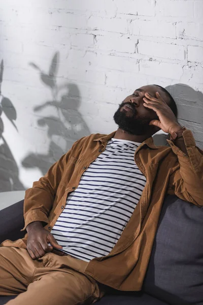Uomo afroamericano seduto sul divano con gli occhi chiusi — Foto stock