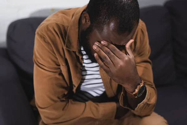 Focus selettivo dell'uomo africano americano seduto sul divano con mano sul viso — Foto stock