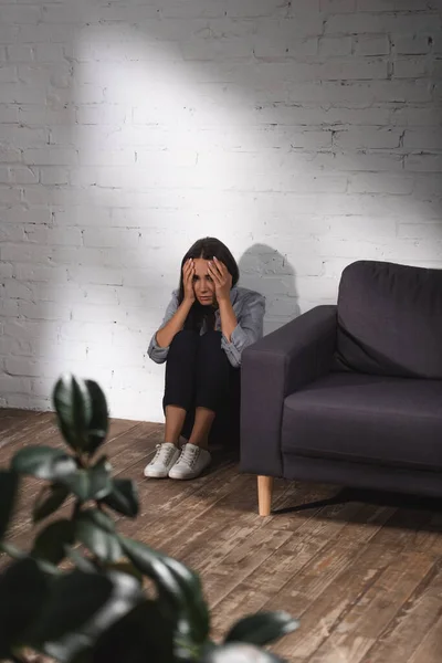 Selektiver Fokus der Frau, die auf dem Boden sitzt und den Kopf berührt — Stockfoto