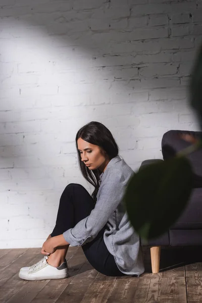 Triste, mujer solitaria sentada en el suelo cerca de la pared de ladrillo en casa, concepto de salud mental - foto de stock