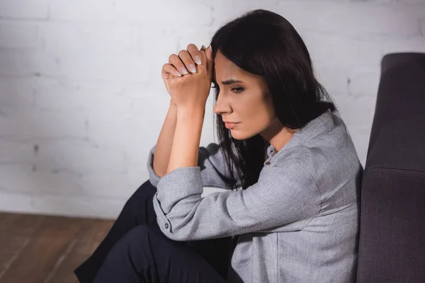 Donna stressata stringendo le mani vicino alla testa mentre seduto a casa, concetto di salute mentale — Foto stock