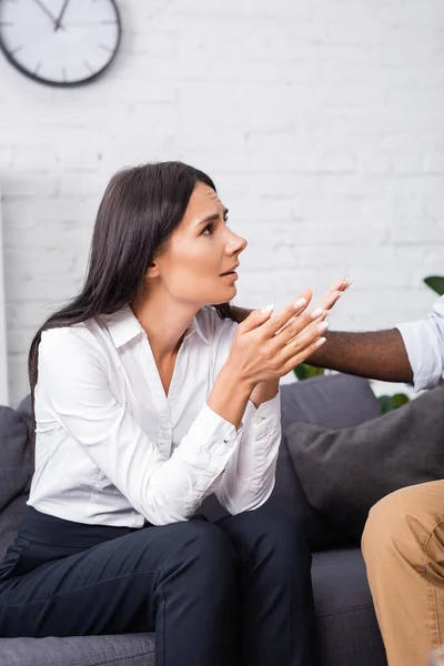 African american psychologist touching stressed patient talking and gesturing while sitting on sofa — Stock Photo