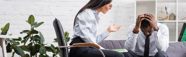 Horizontal image of psychologist gesturing while talking to upset african american patient holding hands on head — Stock Photo