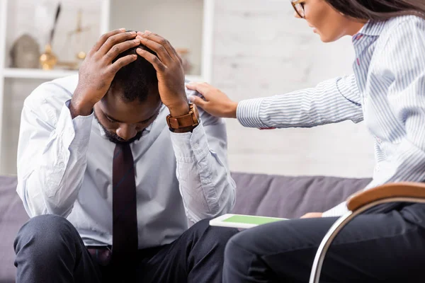 Foco seletivo do psicólogo calmante homem afro-americano frustrado de mãos dadas na cabeça no hospital — Fotografia de Stock
