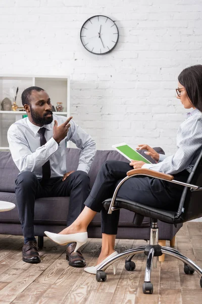 Homem afro-americano estressado gesticulando enquanto conversa com psicólogo segurando tablet digital com tela verde — Fotografia de Stock
