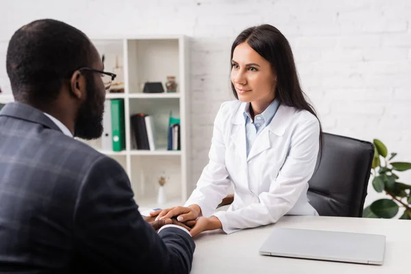 Selective focus of brunette doctor touching hands of african american man in clinic — Stock Photo