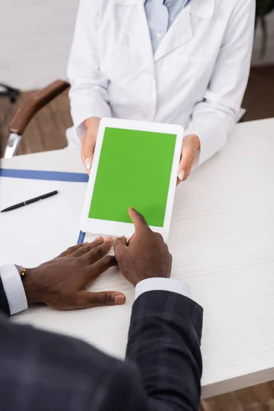 Ausgeschnittene Ansicht eines afrikanisch-amerikanischen Mannes, der mit dem Finger auf ein digitales Tablet mit grünem Bildschirm in der Nähe des Arztes zeigt — Stockfoto