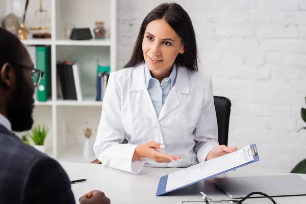 Foyer sélectif de brunette médecin pointant avec la main au presse-papiers avec forme d'assurance près de l'homme afro-américain — Photo de stock