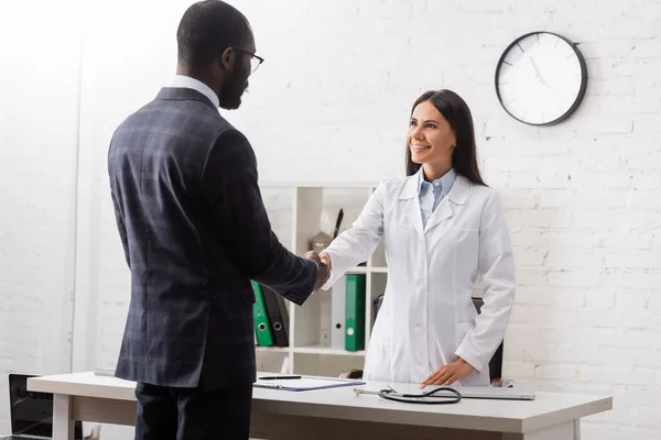 Brunette woman shaking hands with african american patient wearing suit — Stock Photo