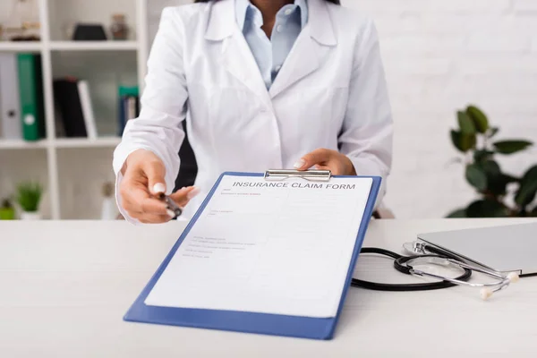 Обрезанный вид врача, держащего страховой полис рядом со стетоскопом на столе — стоковое фото