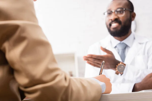 Selective focus of bearded african american doctor in eyeglasses pointing with hand near patient — Stock Photo