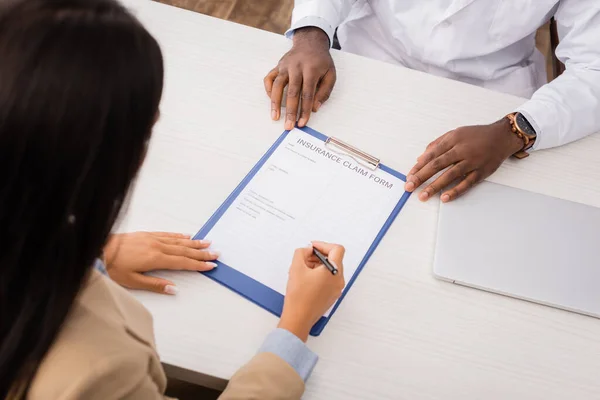 Vue aérienne du patient signant le formulaire de demande de règlement d'assurance auprès du médecin afro-américain — Photo de stock