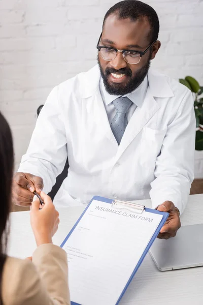 Selektiver Fokus des afrikanisch-amerikanischen Arztes, der dem Patienten Stift und Versicherungsantragsformular gibt — Stockfoto