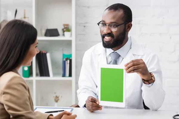 Selective focus of joyful african american doctor holding digital tablet with blank screen near brunette woman — Stock Photo