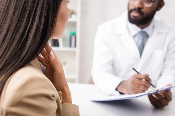 Selective focus of diseased woman touching sore throat near african american doctor holding clipboard — Stock Photo