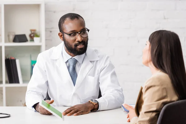 Foyer sélectif du médecin afro-américain dans les lunettes tenant tablette numérique avec écran vert près du patient — Photo de stock