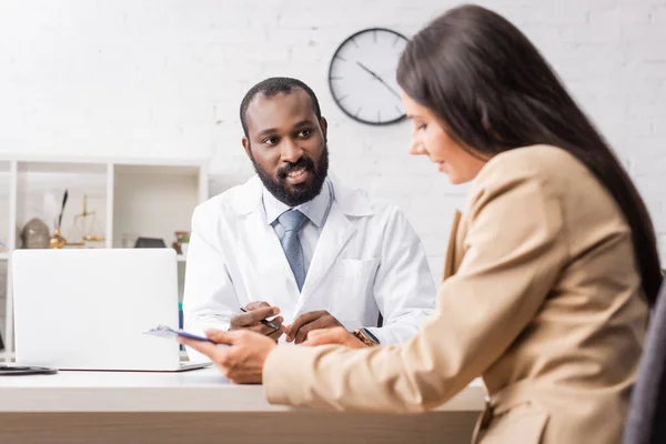 Brunette woman holding clipboard with diagnosis near african american doctor — Stock Photo