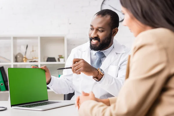 Foyer sélectif de la femme près excité médecin afro-américain pointant avec stylo à l'ordinateur portable avec écran vert — Photo de stock