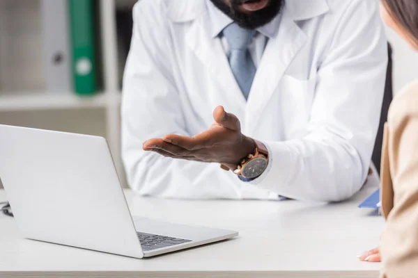 Vista recortada del médico afroamericano apuntando con la mano a la computadora portátil cerca del paciente - foto de stock