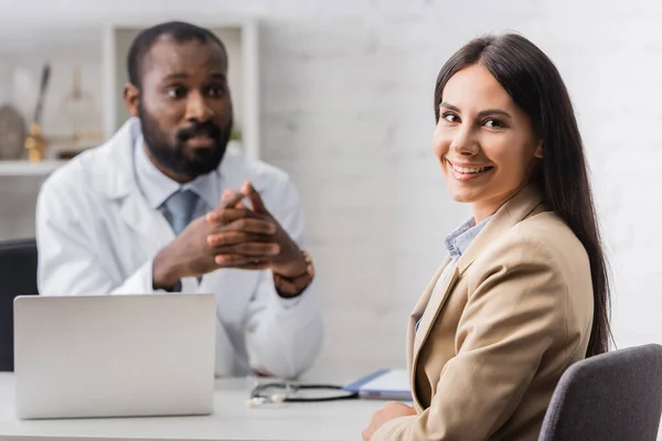 Selektiver Fokus des freudigen Patienten, der in die Kamera in der Nähe eines amerikanischen Arztes blickt — Stockfoto