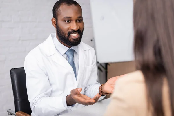 Selektiver Fokus einer Frau in der Nähe eines afrikanisch-amerikanischen Arztes, die am Arbeitsplatz spricht und gestikuliert — Stockfoto