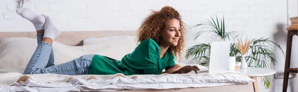 Colpo panoramico di donna dai capelli rossi utilizzando il computer portatile mentre sdraiato sul letto — Foto stock