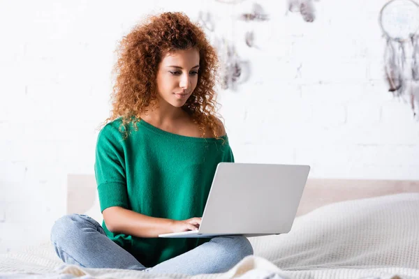 Foco seletivo da mulher encaracolada usando laptop na cama em casa — Fotografia de Stock