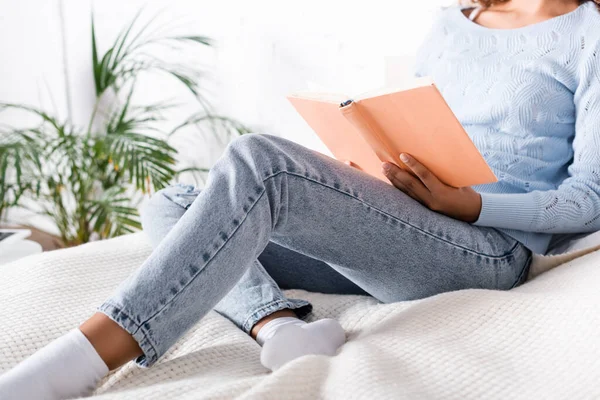 Vista cortada de mulher em jeans e meias livro de leitura na cama — Fotografia de Stock