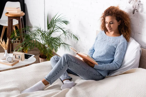 Frau liest Buch neben Kopfhörern und digitalem Tablet auf Couchtisch — Stockfoto