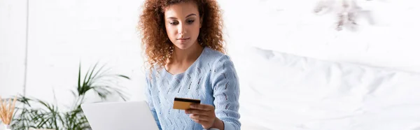 Cultura panorâmica da mulher de cabelos vermelhos segurando cartão de crédito durante compras on-line em casa — Fotografia de Stock