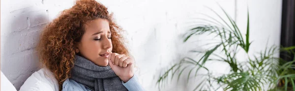 Foto panorámica de mujer en bufanda tosiendo en casa - foto de stock