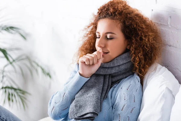 Lockige Frau in Schal und Pullover hustet auf dem Bett — Stockfoto