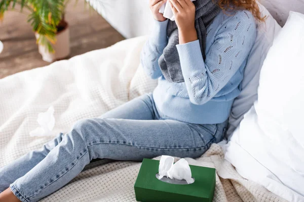 Vista ritagliata della donna malata che tiene il tovagliolo vicino alla scatola sul letto — Foto stock