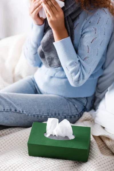 Focus selettivo di scatola con tovaglioli sul letto vicino a donna malata in maglione e sciarpa — Foto stock