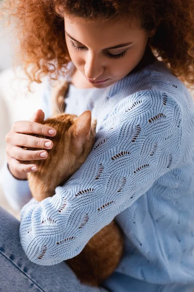 Selective focus of curly woman in sweater hugging ginger cat — Stock Photo