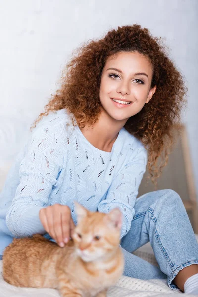 Selektiver Fokus der rothaarigen Frau im Pullover, die in die Kamera in der Nähe der Katze zu Hause schaut — Stockfoto