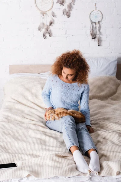 Selective focus of woman touching cat while sitting near smartphone on bed — Stock Photo