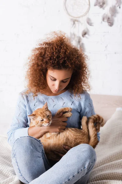 Вибірковий фокус червоної волохатої жінки тримає таббі кішку, сидячи на ліжку — стокове фото