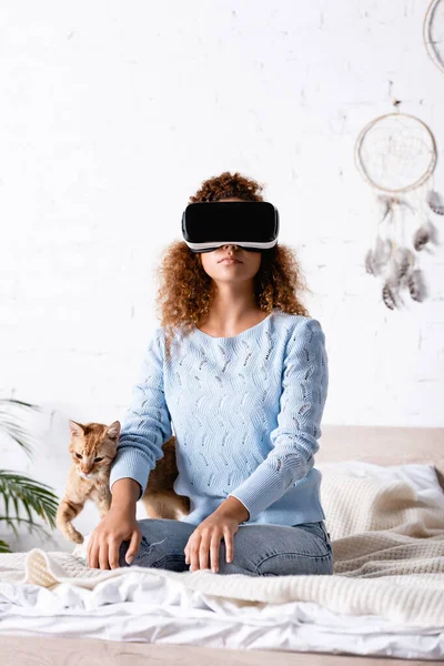 Selektiver Fokus der Frau im vr-Headset, die auf dem Bett neben gestromter Katze sitzt — Stockfoto