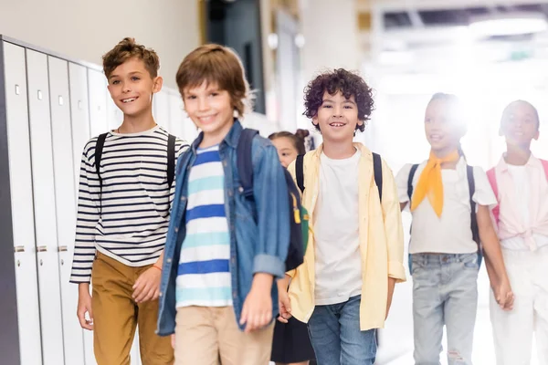 Selective focus of multicultural classmates walking along corridor in school — Stock Photo