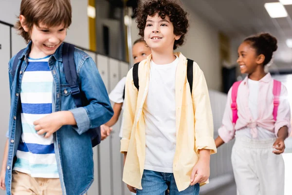 Excited multicultural schoolchildren walking along school corridor — Stock Photo