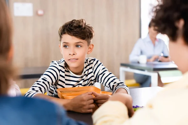 Selective focus of schoolboy sitting in school eatery near classmates — Stock Photo