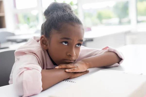 Ennuyé afro-américaine écolière assis au bureau avec la tête sur les mains pendant la leçon — Photo de stock
