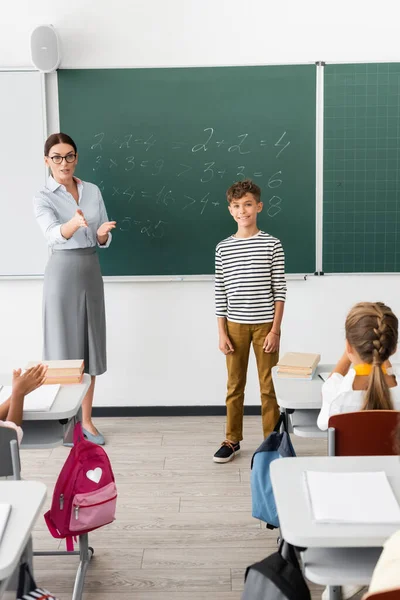 Professeur pointant avec la main tout en se tenant près de l'écolier et tableau avec des équations — Photo de stock