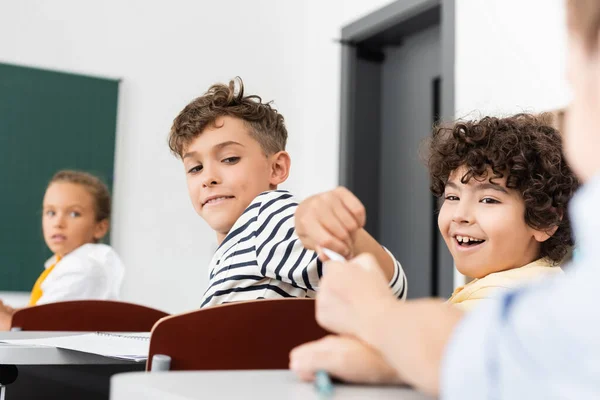 Cropped view of pupil passing note to schoolboy near multicultural classmates during lesson — Stock Photo