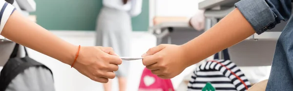 Cropped view of schoolboy passing note to classmate while teacher standing at chalkboard, horizontal image — Stock Photo