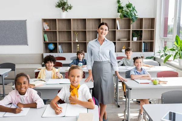 Maestro y alumnos multiétnicos mirando a la cámara en el aula durante la lección — Stock Photo